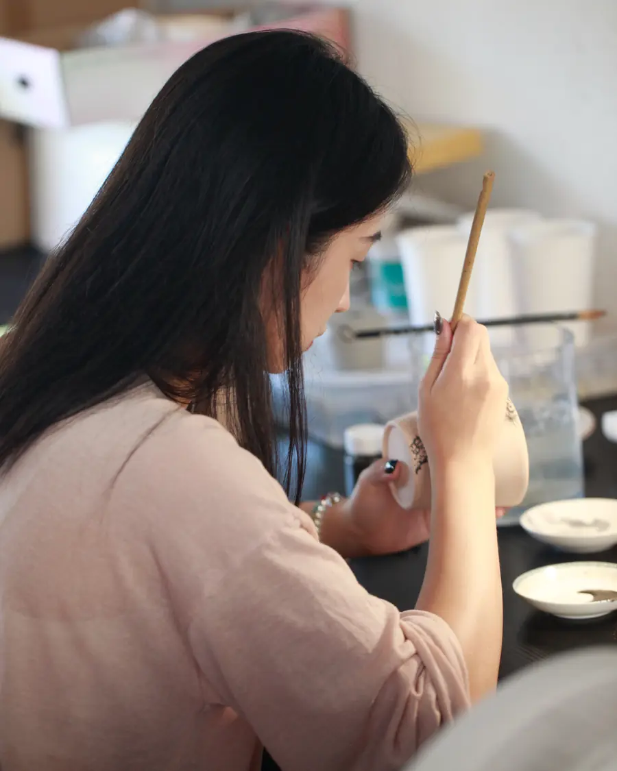 At the studio bench, carving a cup held in one hand