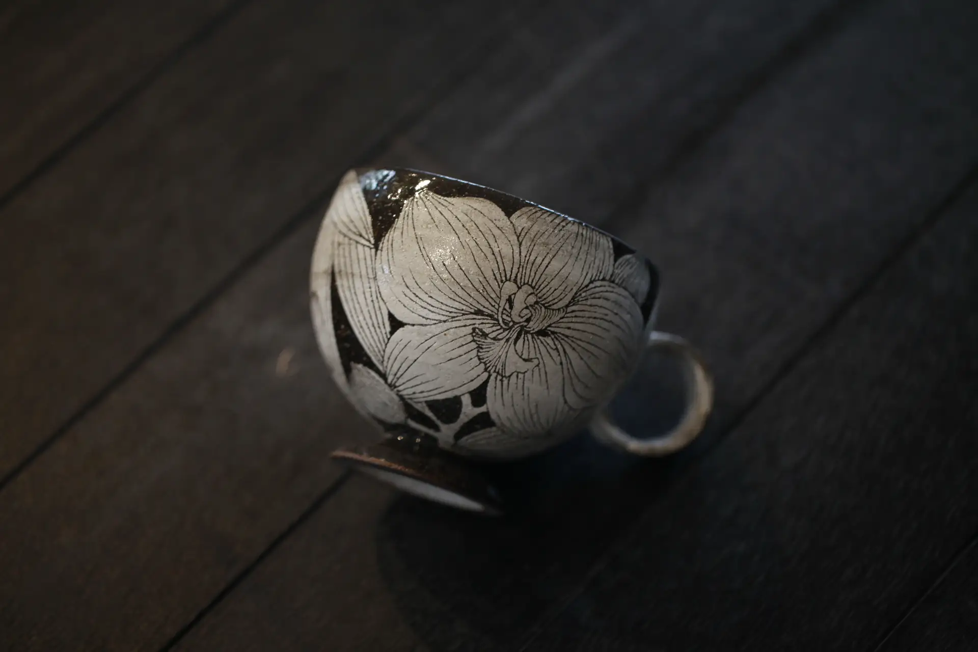 A hand-carved amaryllis teacup resting on dark wood in raking light