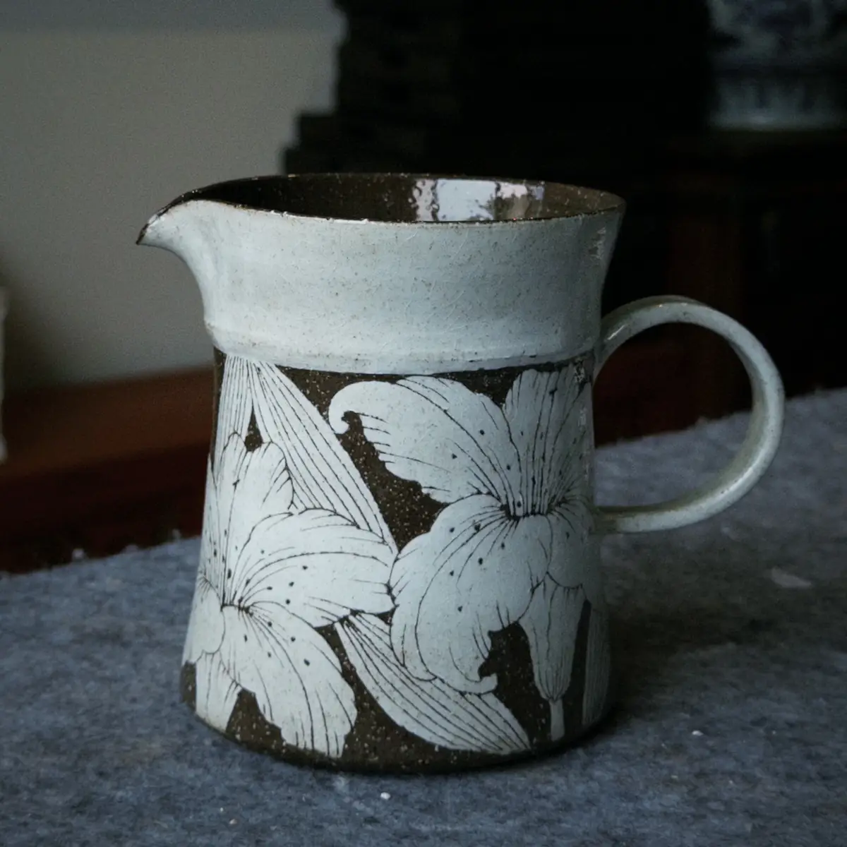A speckled stoneware pitcher with carved lilies, in the studio's evening light
