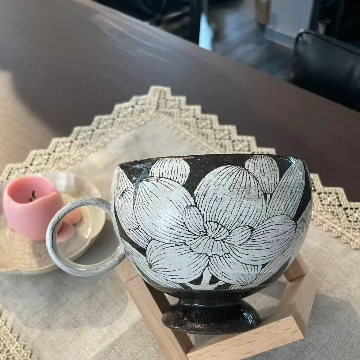 A wide dark stoneware cup on a pedestal foot, white blossoms carved all round the bowl, a round loop handle at the left